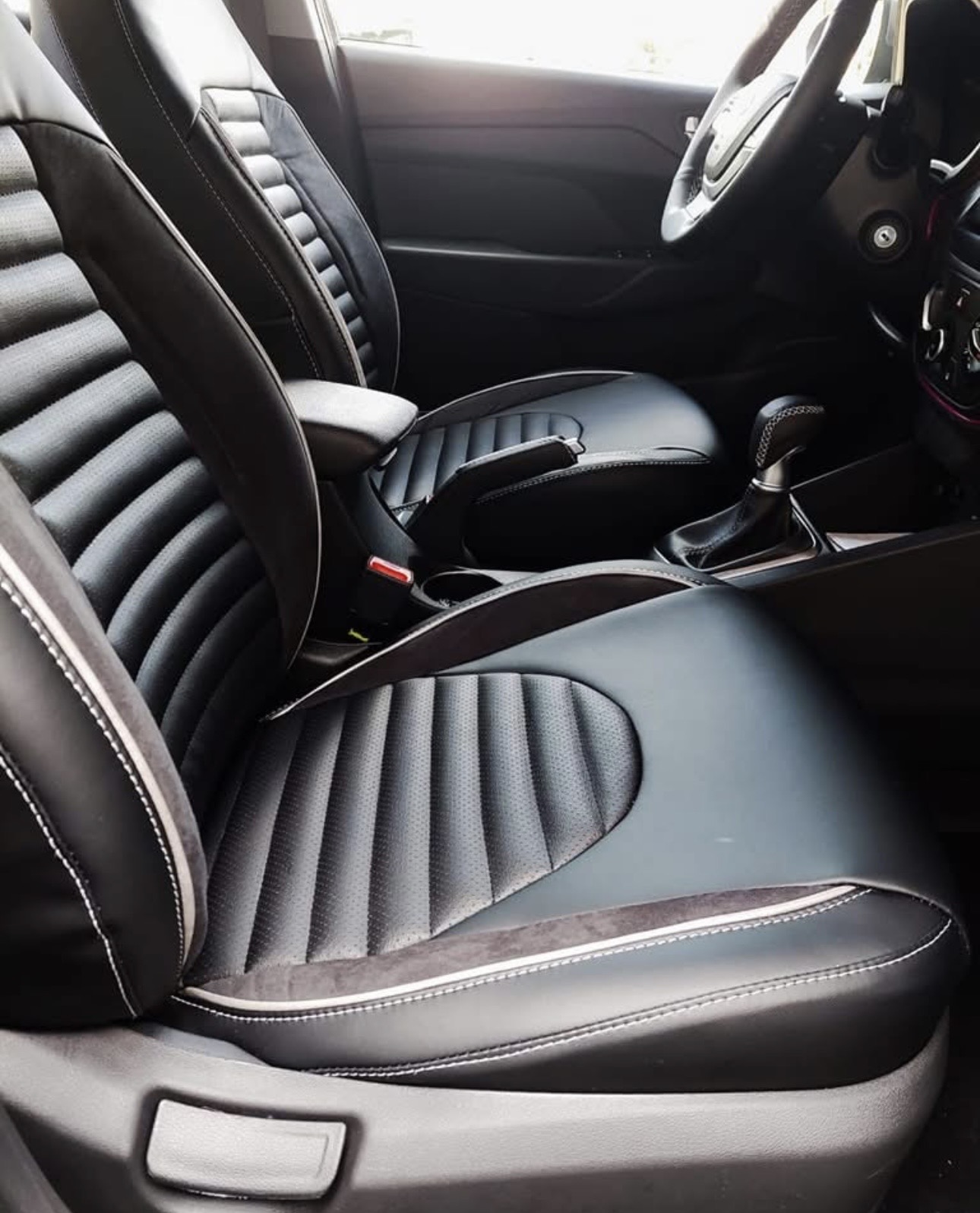 Interior delantero de coche tapizado en piel negra con franjas verticales, alcántara y costura clara
