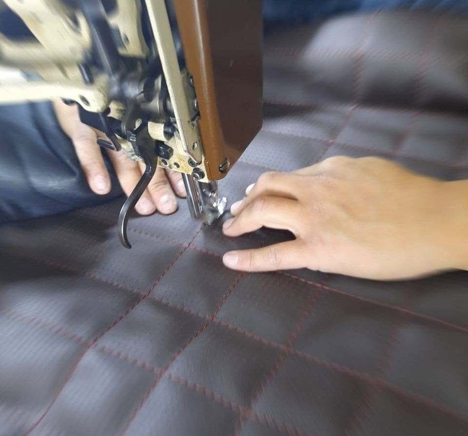Tapicero cosiendo piel en máquina de costura industrial en el taller Euro Asientos