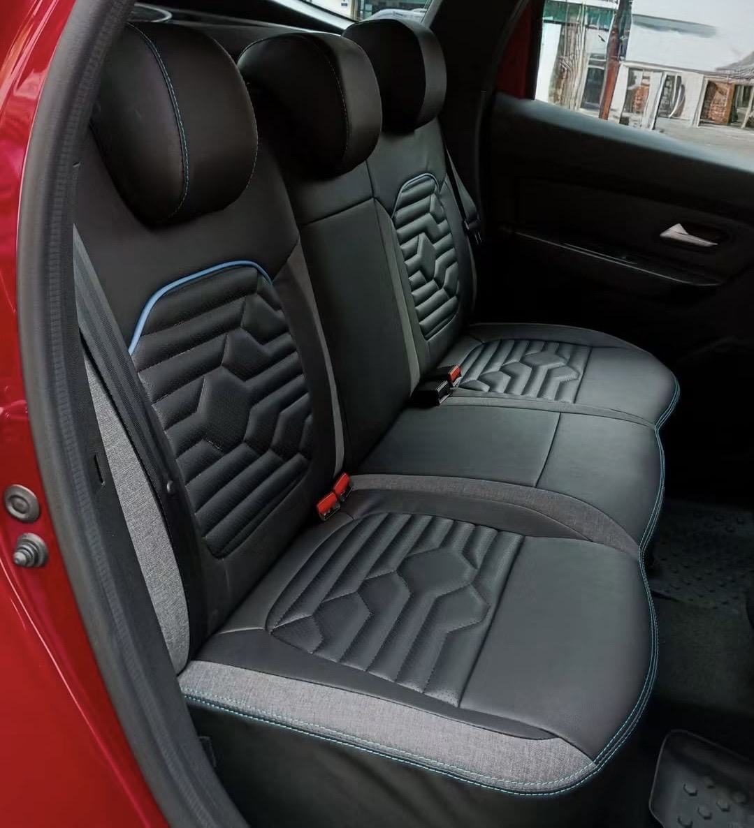 Asientos traseros de coche tapizados en piel negra con relieve geométrico y costura azul, vistos desde la puerta